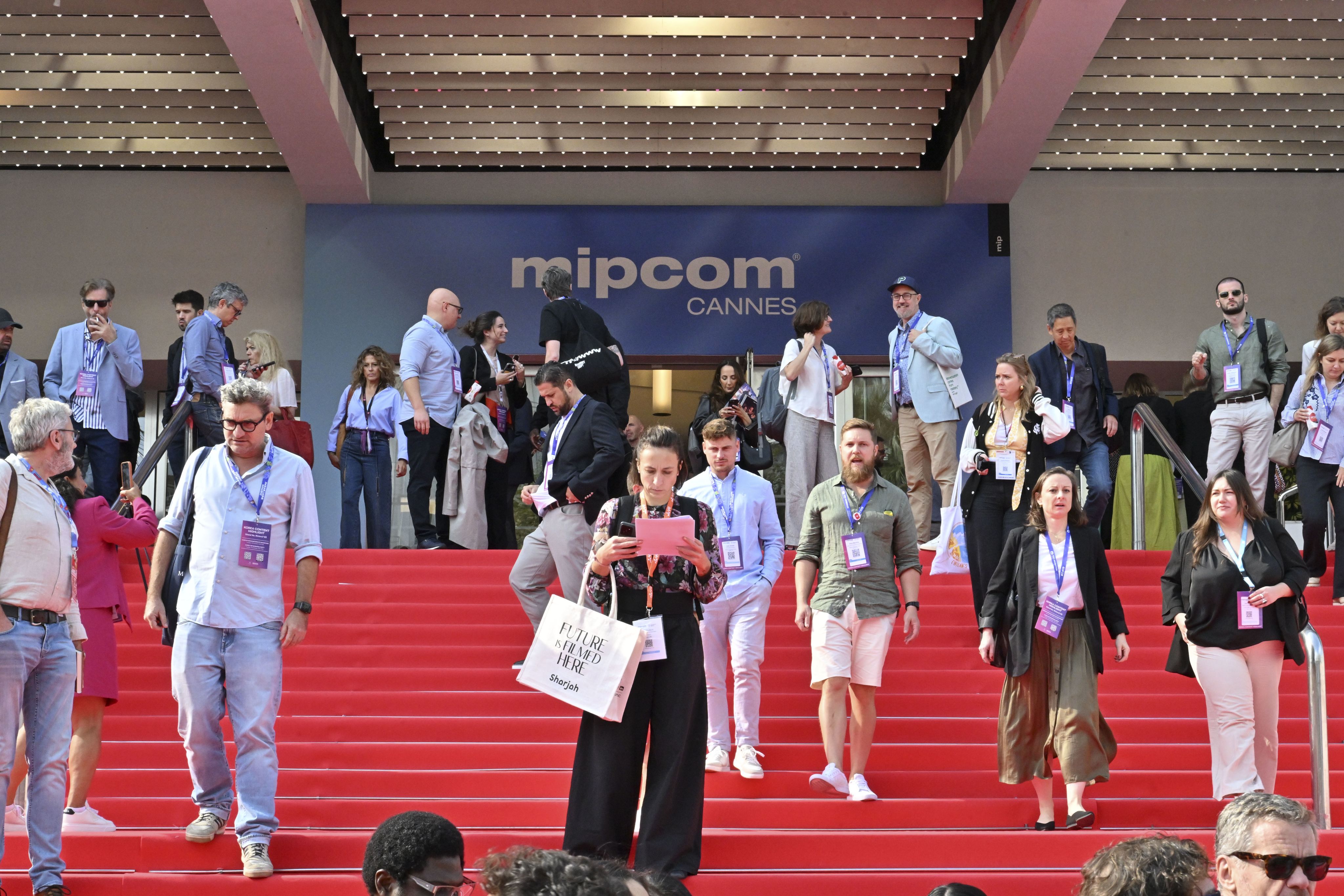 A speaker presents on a large stage with a screen.